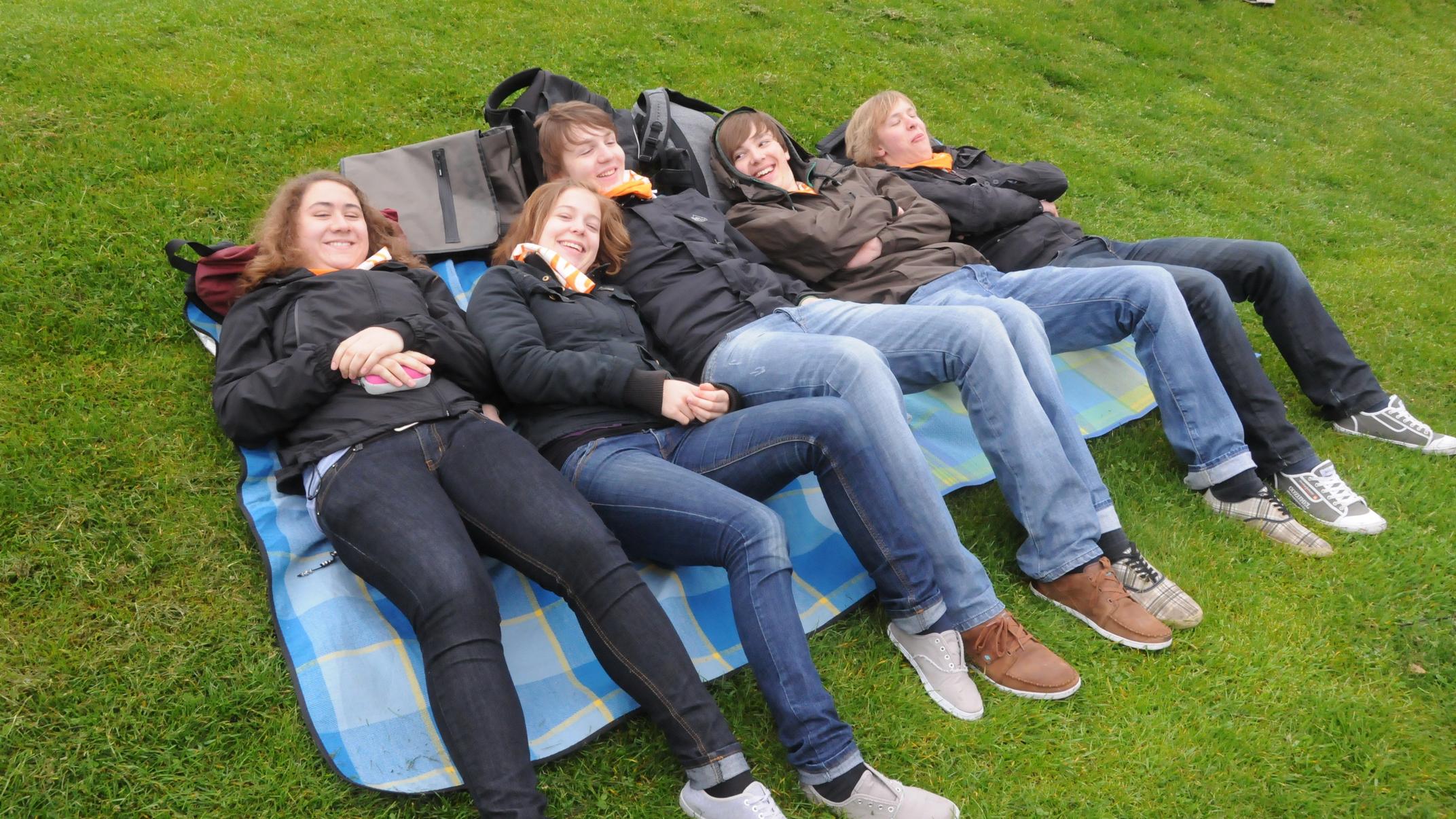 Jugendlche liegen gemeinsam auf Matten auf dem Boden und freuen sich